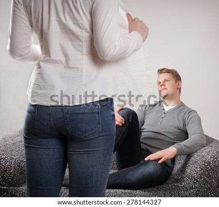 woman taking off blouse while man sitting expectantly on sofa