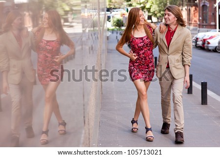 Fashionable happy young couple of a handsome man with long hair and attractive woman walking on the street holding hands
