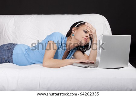 Tired young business woman on bed working on  a laptop. Part of photo series. Studio shot