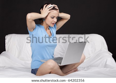 Unhappy young business woman on bed with a laptop, gesturing trouble. Part of photo series. Studio shot