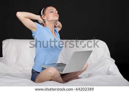Tired young business woman on bed with  a laptop, stretching. Part of photo series. Studio shot