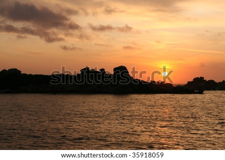orange sunset with a round sun and rocks in the mediterranean sea