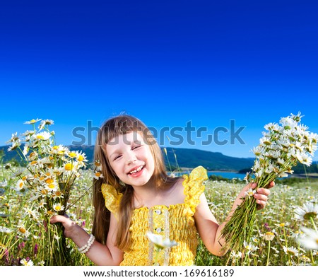 Little beautiful girl holding bouquet of daisies standing in field on blue sky background