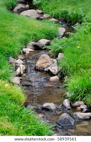 River water flowing past rocks and stones in green meadow