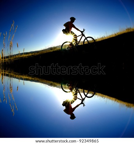 Mountain biking up a trail in the mountains silhouetted reflection in water