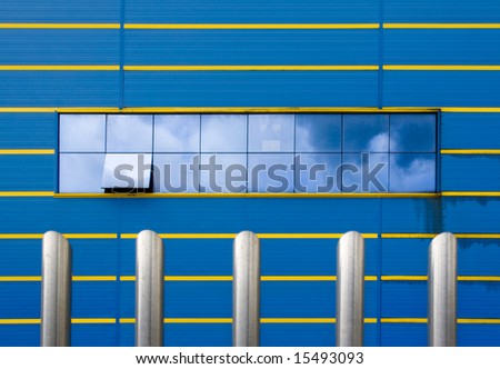 modern blue facade with horizontal lines in yellow. In the middle of the facade a large window reflecting the sky in similar tones to the wall. One of the windows half-open. .