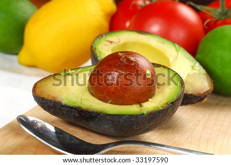 Extreme close-up image of avocado cut on half with some more fruit and veggies in background