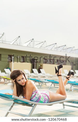 gorgeous brunette girl with sexy long legs wearing black heels sitting on pool chair in bright sunny day