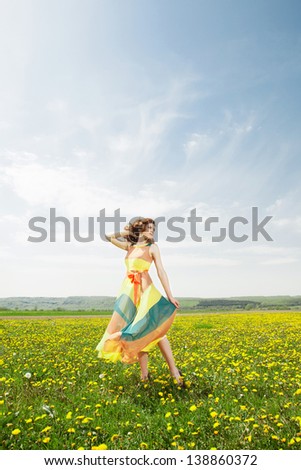Beautiful young girl in flower field wearing colorfull long dress in sunny day