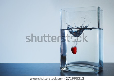 Raspberry dropped into square shaped glass container with water