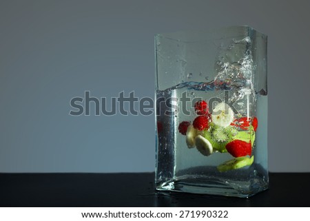 Mixed fruit slices dropped into square shaped glass container with water