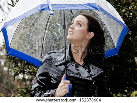 Young woman in shiny black raincoat  looks anxiously at the wet weather