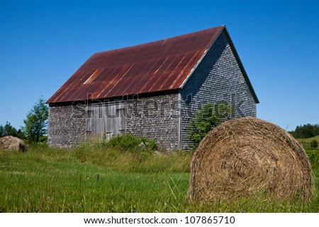 Wood-shingled barn with a red rusted metal roof in New Brunswick, Canada, under a clear blue spring sky