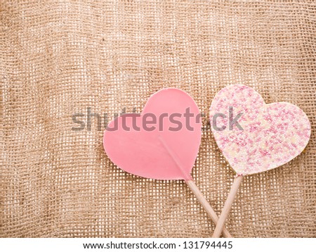 greeting card for Valentine\'s Day with chocolate hearts symbol lollipops with needle on fabric sack texture background