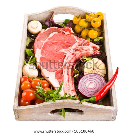 meat - a big piece. beef on the bone,  lies in a wooden box, decorated with greens and vegetables  isolated on a white background.