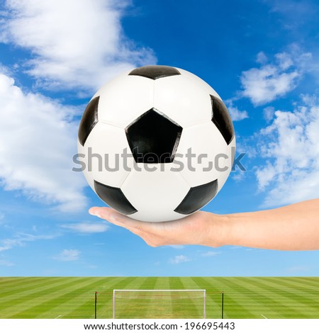 Soccer ball in hand with soccer field and blue sky background