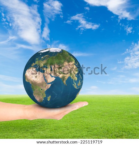 Green Earth concept,hand holding earth against green field and blue sky background.Elements of this image furnished by NASA