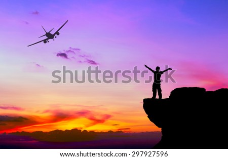 Silhouette of a man on the rock and silhouette commercial plane flying at sunset