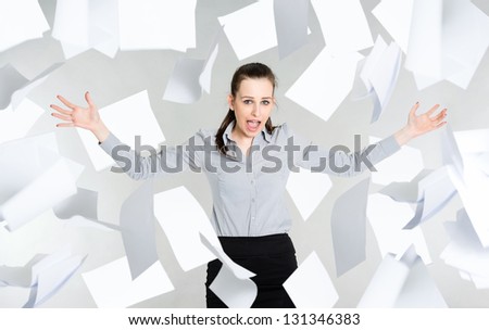 Frustrated young businesswoman with falling paper documents, gray background