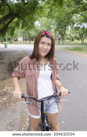 Rejoicing happy woman with mini bicycle in summer or spring forest. Asian female model.
