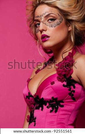 sexy woman with mask on face with creative face art on pink background