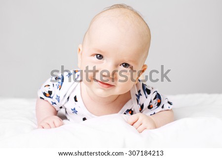 Shot of an adorable, little caucasian boy laying on bed and smiling. He is looking straight into camera.