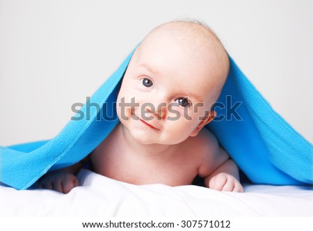 Portrait of a smiling happy caucasian baby boy under blue blanket having fun. Studio indoors shoot isolated over light grey background.