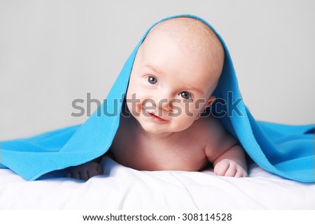 Portrait of  cute, curious, smiling happy caucasian baby boy under blue blanket having fun.