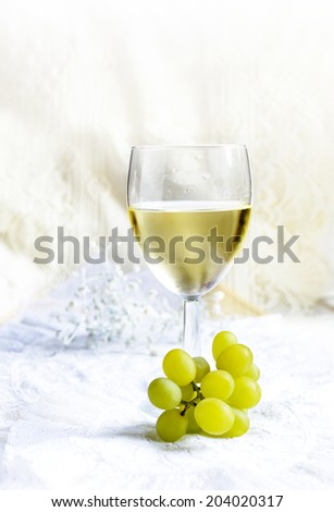 Chilled white wine in a glass with white grapes against a light background. Copy space.