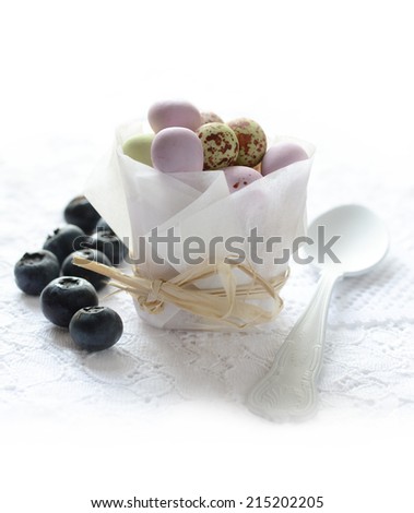 Chocolate Easter mini-eggs in a paper packet tied with raffia with blueberries against a white background. Copy space.