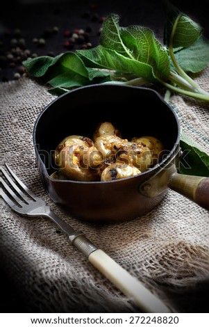 Freshly cooked garlic butter mushrooms tapas with sage leaves in a antique copper pot shot in natural light. The perfect image for your tapas menu cover design.