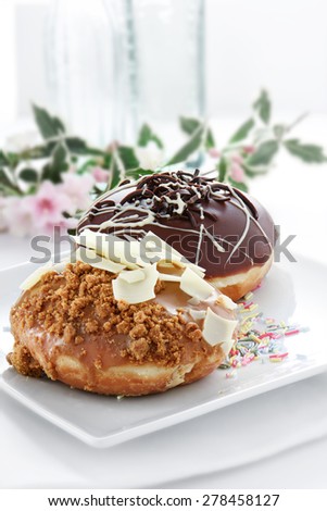 Two delicious donuts against a bright background with copy space. One covered in thick dark chocolate the other with white chocolate and caramel crumble.