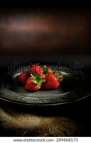 Summer strawberries in a rustic antique setting with selective, creative lighting against dark. An original concept image for your dessert menu cover design. Copy space.