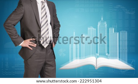 Businessman in suit standing and holding hands on hips. Glowing wire-frame buildings on open empty book as backdrop