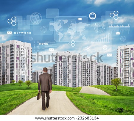 Businessman in suit walking along road through green hills. City of tall buildings in background. Charts and other virtual items in sky. Business concept