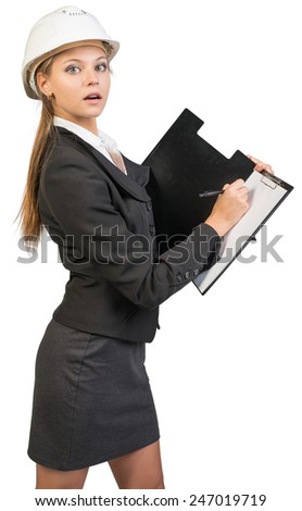 Businesswoman wearing hard hat, writing on blank clipboard, looking at camera. Isolated over white background
