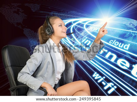 Businesswoman in headset sitting on office chair, touching spot of light with rays around, smiling. Beside is Globe surrounded by light streams of communication. World map composed of digits as