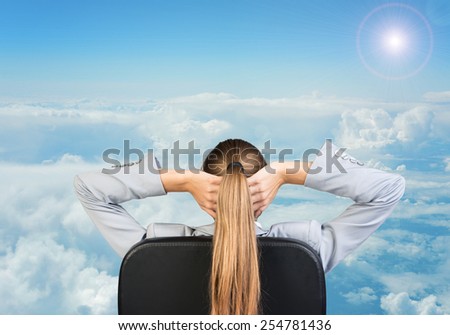 Businesswoman sitting on office chair with hands clasped behind her head. Sky with clouds as backdrop