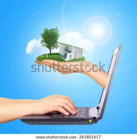 White house in hand with green roof of screen laptop. Hands typing on keyboard. Background sun shines brightly on right. Blue sky