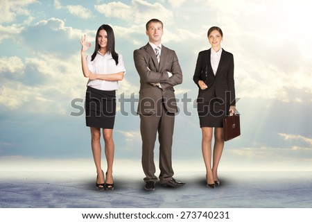Team leader stands with coworkers in background and in looking at camera on abstract background