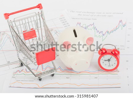 Shopping cart with piggy bank and alarm clock on isolated white background with graphs