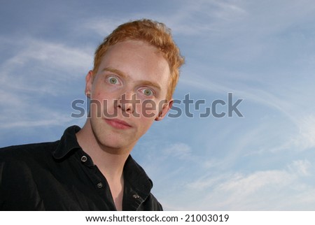 A bizarre young man staring wide-eyed against blue sky.