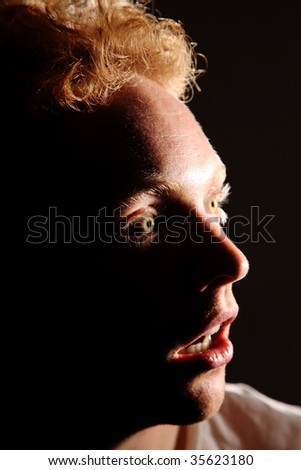 A redhaired, young man looking into the light with eyes wide open.
