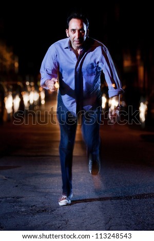 Man running away at night in the middle of a street with car headlights chasing him