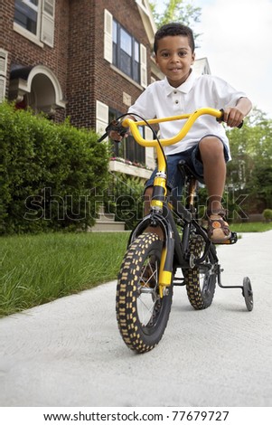 Young boy riding his first bicycle with training wheels (vertical)