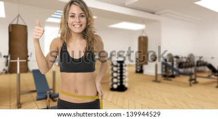 Happy young woman measuring her waist, with a gym club at the background
