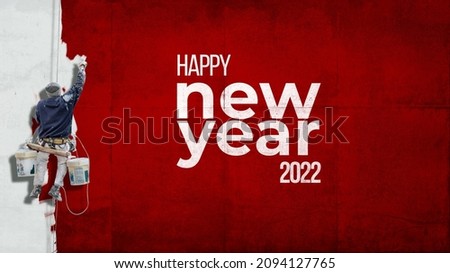 Building painter hanging from harness painting a wall with the words Happy New Year 2022