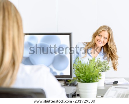 Two female coworkers at the office, sitting face to face in an open space