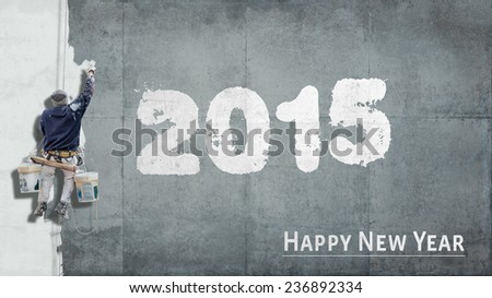Building painter hanging from harness painting a wall with the words Happy New Year 2015