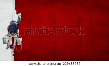 Building Painter hanging from harness painting a wall in red with lots of copy space for your own, message